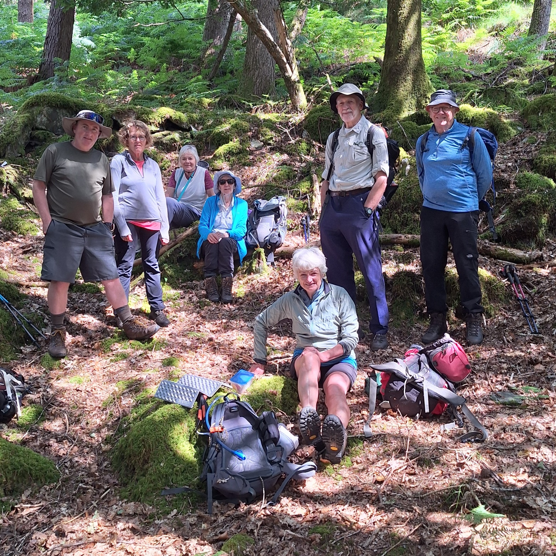 Group of hikers posing in a lush forest, backpacks and trekking poles on rocky ground.